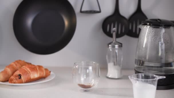 Morning rituals, womans hand makes coffee for herself, pours in soluble grains, pours boiling water from kettle during breakfast in kitchen — Stock Video