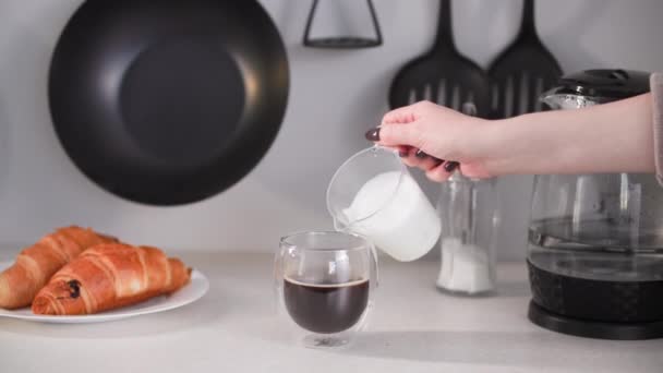 Cappuccino, café preto revigorante quente em copo de vidro com duplo fundo derramando leite espumado enquanto toma café da manhã na mesa da cozinha — Vídeo de Stock