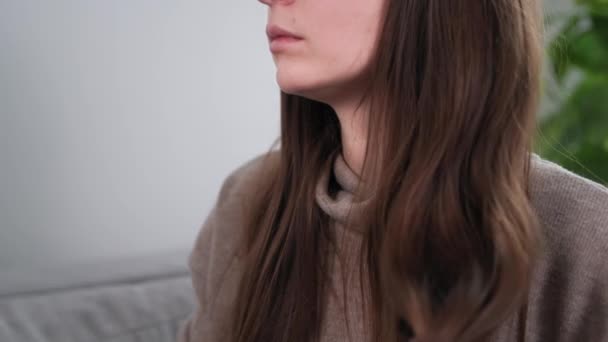 Péče o vlasy, mladá dívka česání její dlouhé zdravé vlasy hřebenem, zatímco sedí na gauči doma — Stock video