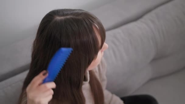 Очаровательная девушка с помощью расчесывания ее длинные волосы, сидя на диване дома, вид сверху — стоковое видео