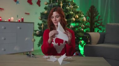 blog paper snowflakes, happy girl blogger tells how to make craft for New Year decor while sitting at home near a Christmas tree, webcam view