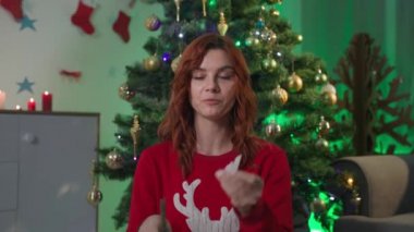 online learning to craft paper snowflakes, female blogger with scissors cuts out the decor for New Year interior while sitting at home near the Xmas tree, webcamera view