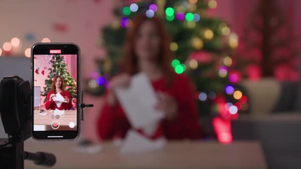 Diy new year, blogger with scissors shows how to cut snowflake out of paper for christmas decor in front of a smartphone camera near xmas tree — Vídeo de Stock