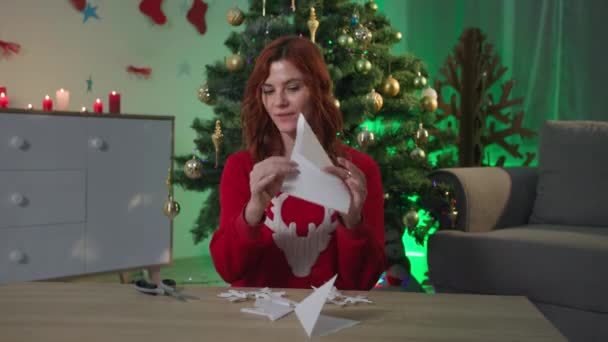 Блог паперові сніжинки, щаслива дівчина-блогер розповідає, як зробити ремесло для новорічного декору, сидячи вдома біля ялинки, вид на веб-камеру — стокове відео