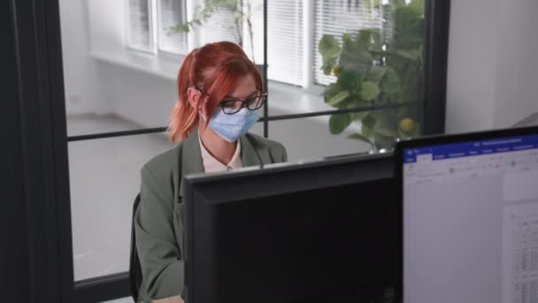 Werk pandemie, charmante vrouwelijke kantoormedewerker met een masker op haar gezicht werkt op de computer het nemen van voorzorgsmaatregelen na het openen van lockdown — Stockvideo