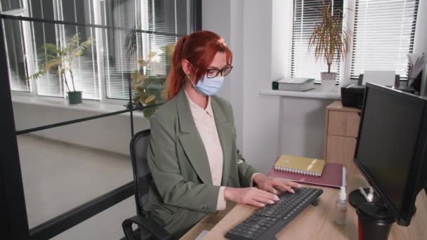 Vrouwelijke werknemer draagt een medisch masker voor virusbescherming en -behandeling behandelt het toetsenbord met antisepticum om de verspreiding van het coronavirus te voorkomen — Stockvideo