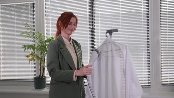 Technologia wygładzania odzieży z ręcznym parownikiem, młoda kobieta wykorzystuje nowoczesne urządzenia gospodarstwa domowego i używa pary do żelaza tkaniny na koszuli, stojąc w pokoju przed oknem — Wideo stockowe