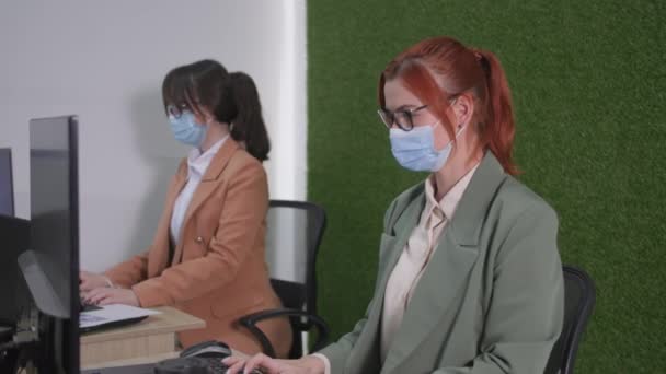 Koronawirus pracy, młode pracownice noszące okulary maski medycznej pracują przy komputerowym podejmowaniu środków ostrożności w celu ochrony przed wirusami i zakażeniami w biurze — Wideo stockowe