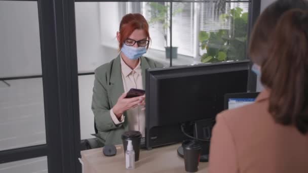 Красива жінка в медичній масці розмовляє з працівницею-жінкою, вживаючи запобіжні заходи в офісі після початку роботи і скасування блокування — стокове відео