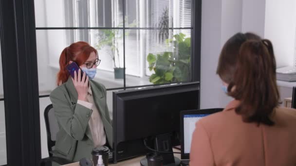 Neue Normen, junge fröhliche Angestellte in medizinischer Maske telefoniert, wirft Papiere in die Höhe und schlägt einen Kollegen mit den Ellbogen, um im Büro gute Nachrichten zu feiern — Stockvideo