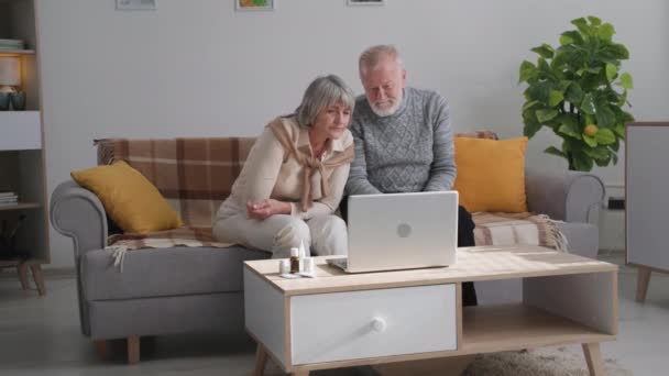 Врач онлайн, пожилая женщина и мужчина с плохим здоровьем общаются с терапевтом по видеосвязи на ноутбуке, сидя дома из-за карантина — стоковое видео