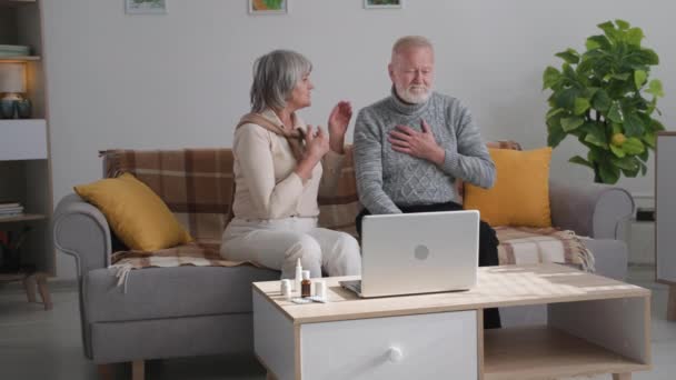 Онлайн-медицина, пожилая женщина и мужчина с плохим здоровьем общаются с врачом по видеосвязи на ноутбуке, сидя дома из-за карантина — стоковое видео