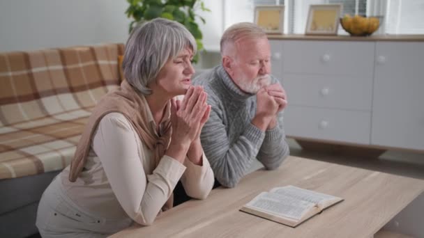 Religione, credenti anziani coppia di sposi inginocchiati con le mani giunte in amore e speranza per Dio mentre in piedi nel soggiorno — Video Stock