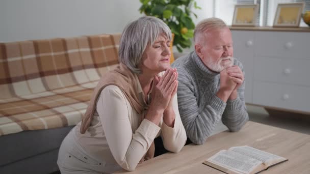 基督徒，可爱的退休人员，心中充满了信心，双手交叉，闭着眼睛跪在客厅里 — 图库视频影像