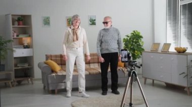 Emekli hobiler, neşeli büyükanneler ve büyükbabalar evdeki rahat odada sosyal ağlar için cep telefonu kamerasıyla dans ederken eğleniyorlar.