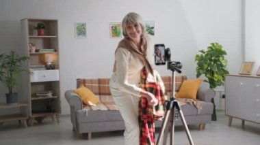 Blog yazma, modern neşeli yaşlı büyükanne ve büyükbaba akıllı telefon kamerasıyla sosyal ağlar için komik videolar çekiyor ve rahat bir odada sihirli numaralar gösteriyor.