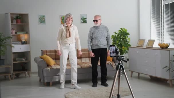 Passe-temps à la retraite, les grands-parents joyeux s'amusent à filmer des danses sur une caméra de téléphone mobile pour les réseaux sociaux dans une chambre confortable à la maison — Video