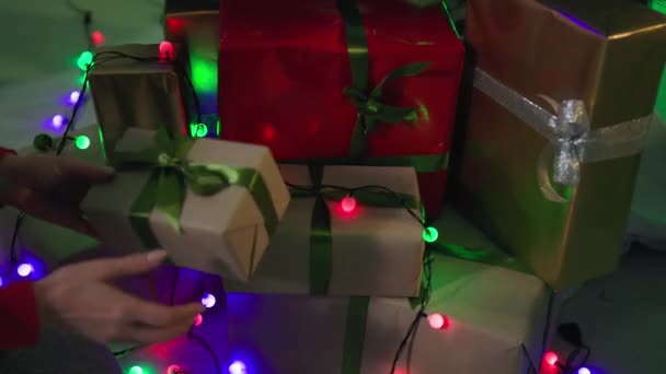 Зимние праздники, заботливая женщина кладет подарки под елку для семьи и украшает гирляндой, крупным планом — стоковое видео