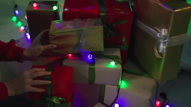 Рождество, любящая женщина складывает красивые подарки под елку, украшает мерцающие гирлянды, праздничная атмосфера — стоковое видео
