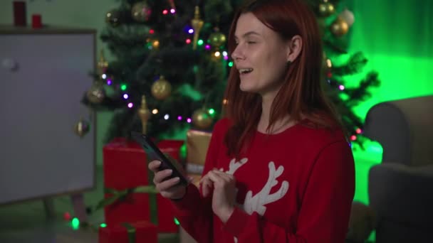 Uśmiechnięta piękna kobieta kupuje prezenty na Nowy Rok dla mojej rodziny w sklepie internetowym, uśmiecha się i pokazuje ekran smartfona z chromatycznym kluczem do kamery — Wideo stockowe