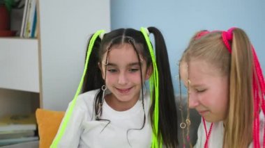 Örgülü şirin kızlar, evde kanepede otururken sosyal ağlarda akıllı telefondan eğlenceli videolar izleyerek eğleniyorlar.