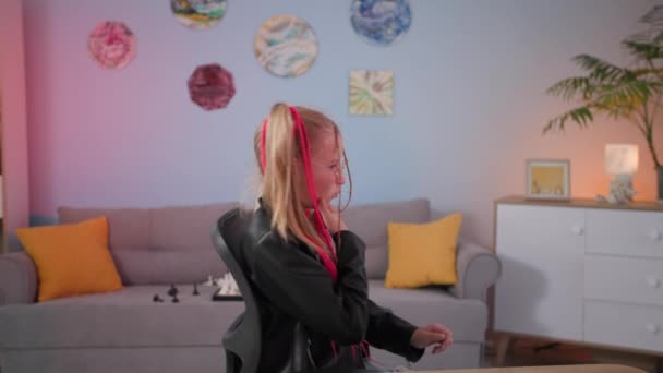 Porträt von stilvollen schönen Teenager-Mädchen mit farbigen Zöpfen dreht sich um und blickt in die Kamera und zeigt die Klasse, während sie in einem schönen und gemütlichen Kinderzimmer sitzt — Stockvideo