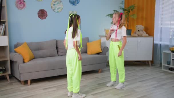 As crianças estão descansando em casa, meninas adoráveis elegantes com tranças coloridas estão aprendendo a dançar para uma multidão flash nas redes sociais em um quarto acolhedor — Vídeo de Stock