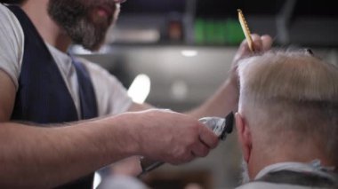 Berber, modern erkek kuaför kuaförde oturan yaşlı bir adama saç kesme makinesiyle saç kesimi yapıyor.