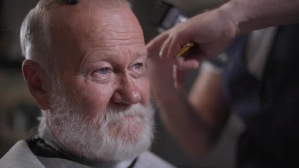 Portret starszego, stylowego mężczyzny z brodą obcina włosy przycinaczem w modnym salonie fryzjerskim — Wideo stockowe