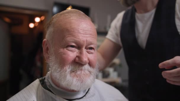 Ritratto di un cliente anziano sorridente mentre taglia e acconcia capelli e barba in un barbiere professionista, cura personale — Video Stock