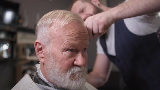 Salão de cabeleireiro, barbeiro profissional corte de cabelo com tesoura e pente para homem idoso elegante na barbearia, close-up — Vídeo de Stock
