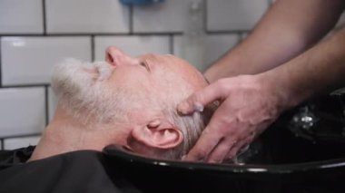 Saç yıkama, profesyonel erkek kuaför kuaförde profesyonel şampuanı olan yaşlı bir erkek müşterinin kafasını yıkıyor.