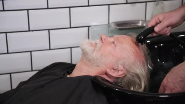 Salone maschile, un parrucchiere maschile lava la testa di un uomo anziano su una sedia professionale con un lavandino da barbiere — Video Stock