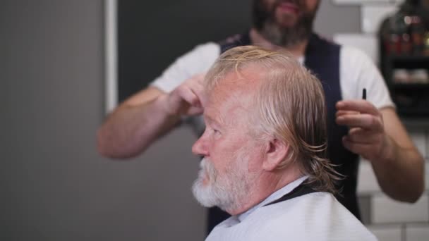 Parrucchiere, barbiere professionista taglia i capelli a elegante cliente anziano maschio in barbiere — Video Stock