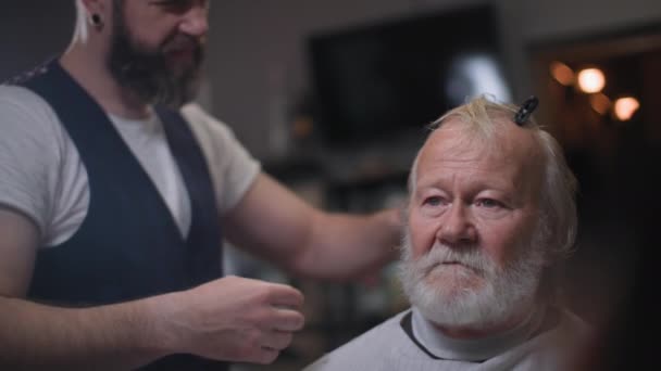 Barbershop, stylish elderly man with gray beard gets haircut at barber in hair salon — Stock Video