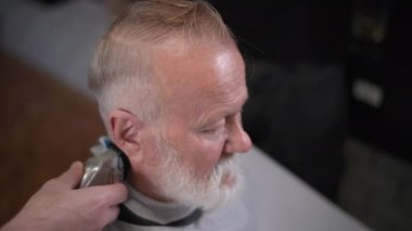 Çekici, sakallı yaşlı adam berber dükkanında modern saç kesimi yapıyor.