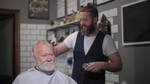 Стрижка волос с триммером, современный мужчина парикмахерская на пенсии стрижка волос и бороду у популярного парикмахера, сидя в кресле парикмахера в салоне — стоковое видео