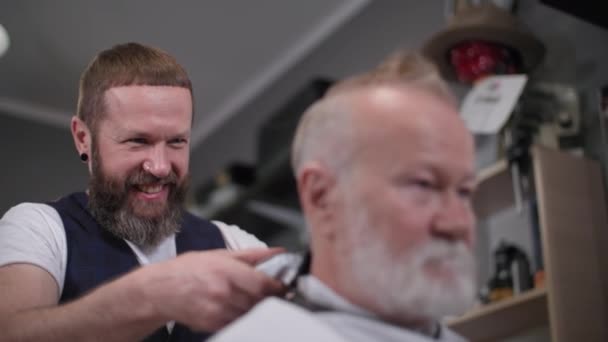 Fryzjer, radosny profesjonalny fryzjer daje fryzurę stylowemu starszemu klientowi w salonie męskim — Wideo stockowe