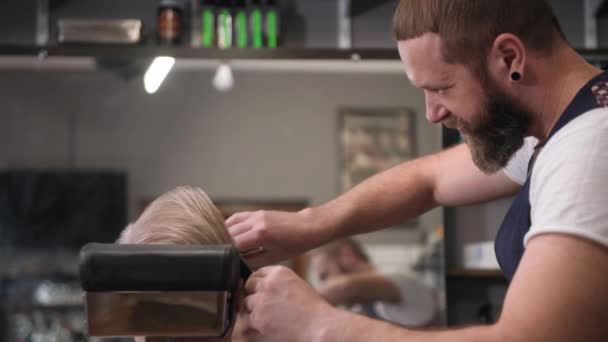 Κομψό επαγγελματικό αρσενικό κουρέας κουρεύει γενειάδα και τα μαλλιά με ψαλίδι και χτένα σε έναν άνδρα με γκρίζα μαλλιά σε ένα σαλόνι — Αρχείο Βίντεο