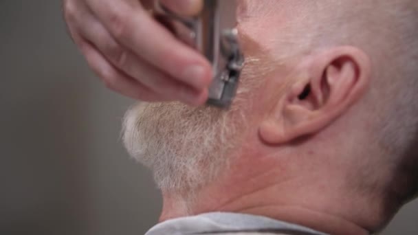 Professionale parrucchiere maschile utilizza strumenti per tagliare e stile capelli e barba a un cliente anziano in un salone — Video Stock