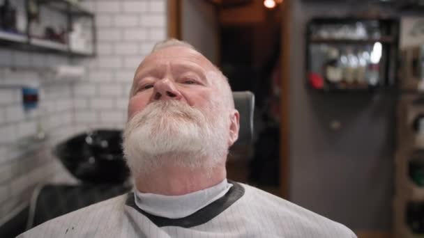 Cura personale, anziano uomo dai capelli grigi si taglia i capelli e la barba con un trimmer in un popolare barbiere, primo piano — Video Stock