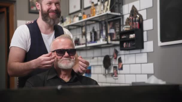 Professionale parrucchiere maschile styling capelli e baffi con la barba a un uomo anziano dai capelli grigi elegante in un barbiere — Video Stock