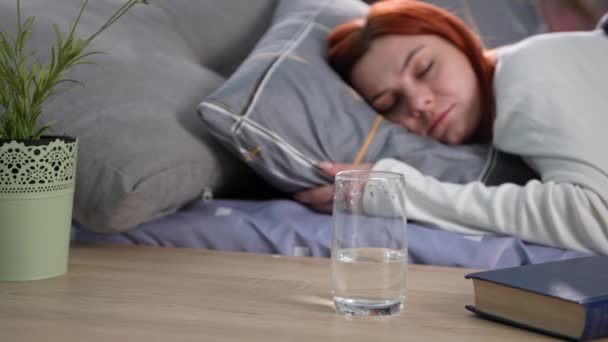 Rituales de la mañana, una joven mujer bebe agua limpia y saludable en un vaso después de despertarse del sueño mientras está acostada en la cama, de cerca — Vídeo de stock