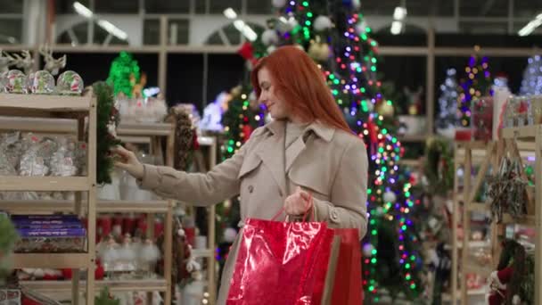 Yeni yıl alışverişi, alışverişi olan mutlu kadın mağazada Noel için ev dekorasyonu için şenlikli süslemeler seçiyor. — Stok video