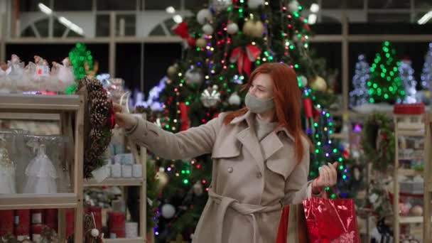 Yüzünde koruyucu maske takan neşeli kadın güvenlik kurallarına uyan aile ve arkadaşlar için yeni yıl tatili hediyeleri seçiyor. — Stok video