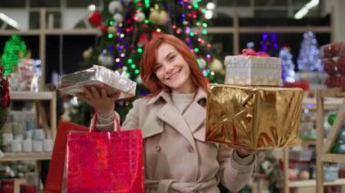 Alışveriş, alımlı genç bir kadın Noel tatilinde ailelerine aldığı hediyelerle seviniyor. Gülümsüyor ve kameraya bakıyor.