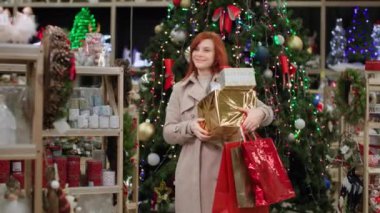 Elinde hediyeler olan mutlu bayan alışverişçi, mağazada rahat bir şenlik ortamı yaratmak için ev dekorasyonunu seçiyor.