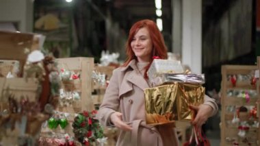 Elinde hediyeler olan hoş bir kadın yılbaşı için mağazadan mal alıyor, gülümsüyor ve kameraya bakıyor.