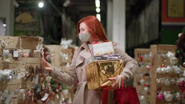 Virüsten ve enfeksiyondan korunmak için maske takan bir kadın, Noel tatili için bir mağazada ev dekorasyonu seçiyor. — Stok video