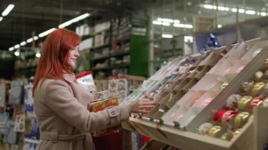 Perakende mağazası, elinde hediyelerle gülümseyen güzel bir kadın süpermarketteki Noel ağacını süslemek için yeni yıl oyuncaklarını seçiyor.